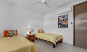 A room with two beds, a ceiling fan, an air conditioning unit, and a door. - Modern Apartment with a Pool (Puerto Vallarta)
