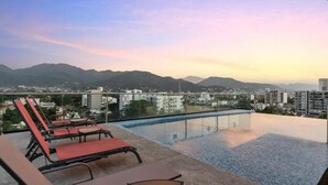 Ein Rooftop-Endlospool mit Liegestühlen, mit Blick auf Stadt und Berge.