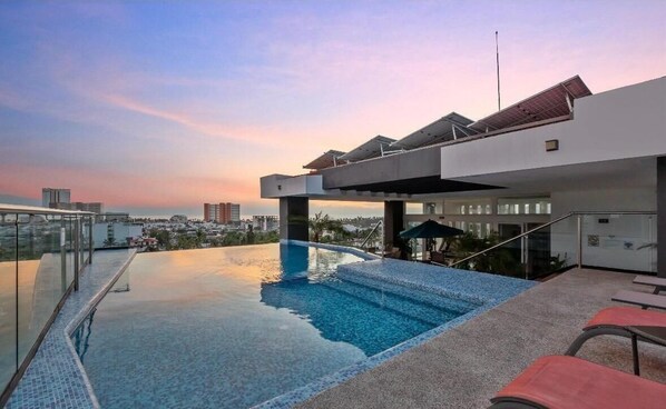 Piscina infinita no terraço com vista para a cidade, área de estar coberta e design arquitetônico moderno.