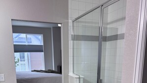 Een moderne badkamer met een douchecabine van glas, een klein nachtkastje en uitzicht op een gebouw van baksteen.