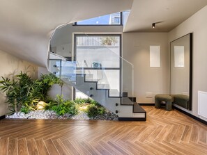Un intérieur moderne avec un escalier en verre, un parquet en bois disposé en chevrons et un petit jardin intérieur.