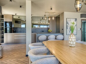 Une cuisine moderne dotée d’appareils électroménagers intégrés, un coin repas avec une table en bois et des chaises rembourrées, ainsi qu’un vase décoratif.