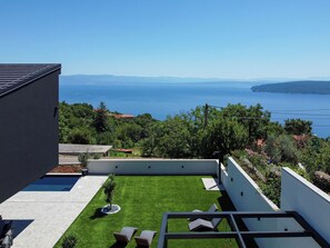 Une terrasse extérieure moderne offrant une vue sur la mer et les montagnes lointaines.