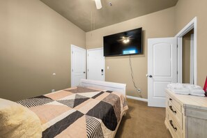 Ein Schlafzimmer mit einem Bett, einem an der Wand montierten Fernseher, einer Kommode und zwei Türen.