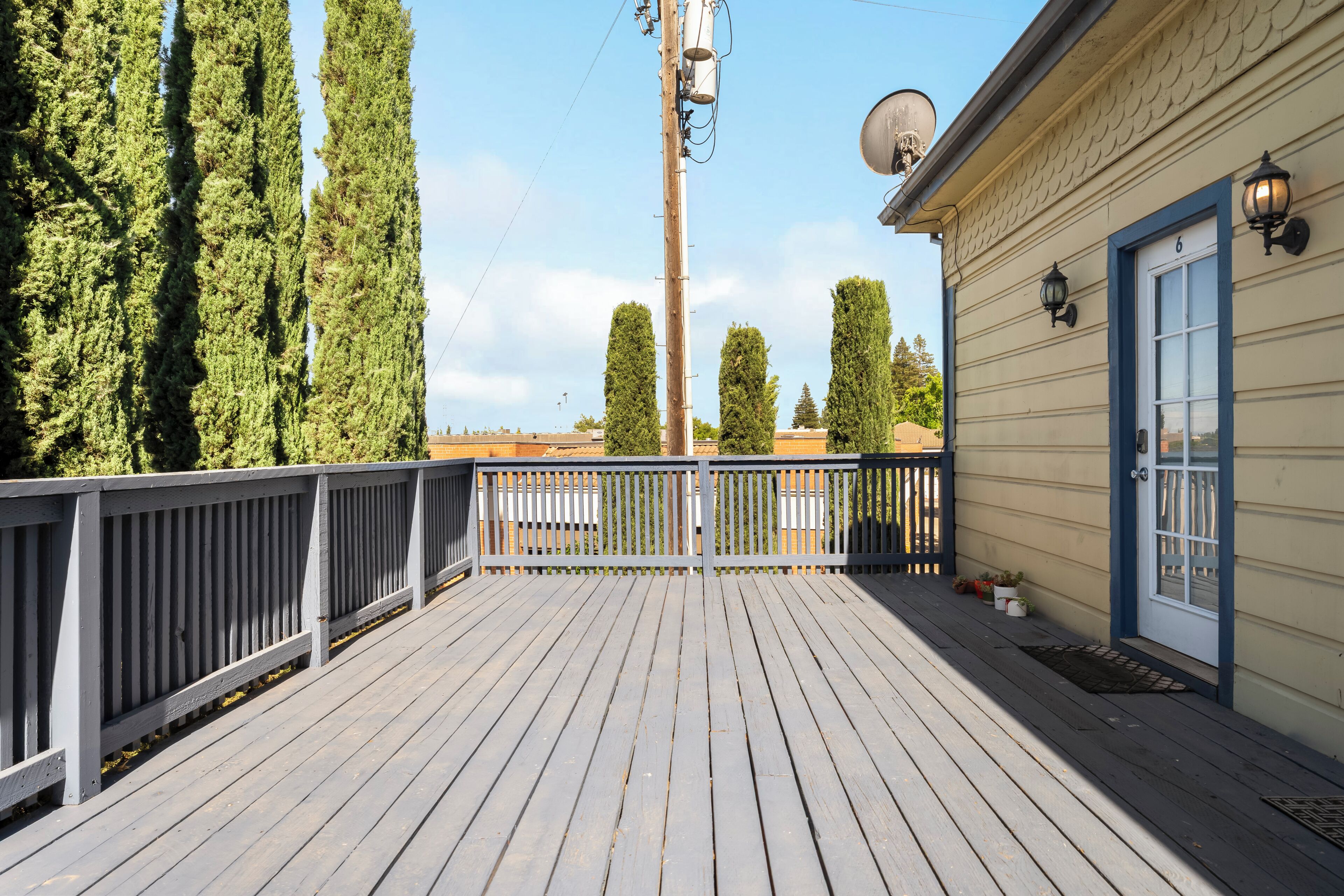 A wooden deck with a railing, a building with a garage door, and tall trees in the background.