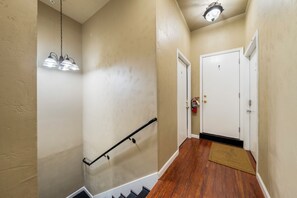 A hallway with a wooden floor, a black handrail, a white door with the number 7, and a ceiling light fixture.