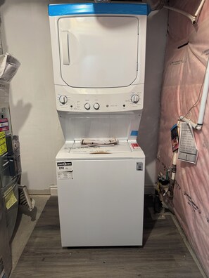 Una lavadora y secadora ENERGYGUIDE blancas en un lavadero pequeño con una cortina rosa y varios objetos en la pared.