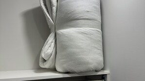 A white pillow on a shelf in a room with a plain wall and a ceiling light.