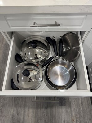 Un cajón con varios utensilios de cocina, incluyendo ollas, sartenes y tapas.