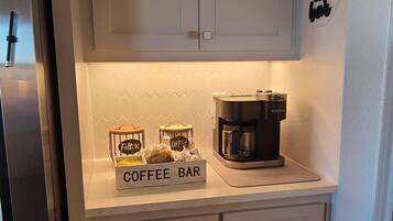 A kitchen with white cabinets, a coffee bar, a coffee maker, and a refrigerator.