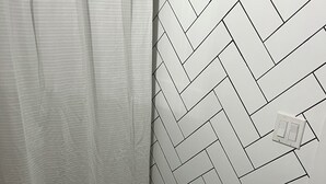 Un bagno con una parete a motivo a spina di pesce, una tenda da doccia bianca, un cesto in vimini e un piccolo sgabello.