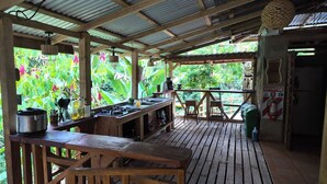 An outdoor kitchen area with a wooden table, a gas stove, and a view of lush greenery. - Finca Secreto Sur, A Hidden Paradise in the Jungle (Carara)