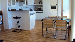 Une cuisine compacte avec un îlot central, un coin repas avec des chaises en osier et un tabouret de bar.
