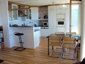 A compact kitchen with a central island, a dining area with wicker chairs, and a bar stool. - Plattas, (Flims Fidaz), 1045 by Interhome (Flims)
