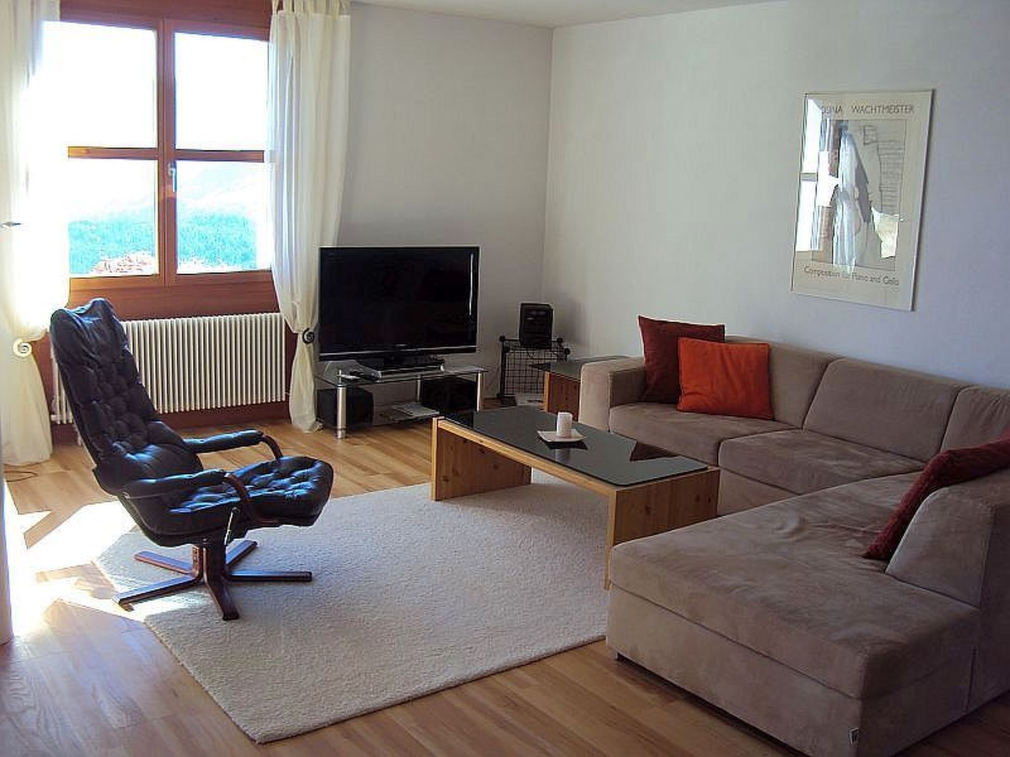 A living room with a leather chair, a sofa, a coffee table, a television, and a radiator.