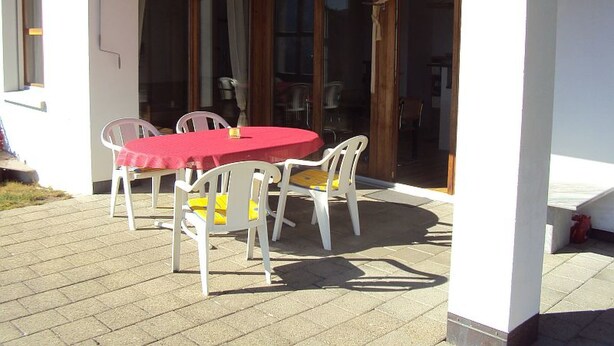 Une terrasse extérieure avec une table ronde et quatre chaises, une nappe rouge et un plafond en bois.