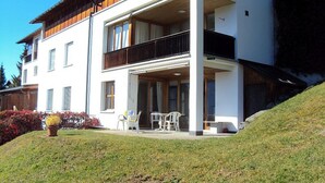 Un bâtiment à deux étages doté d’un balcon, d’un espace extérieur aménagé pour s’asseoir et d’une pente herbeuse.