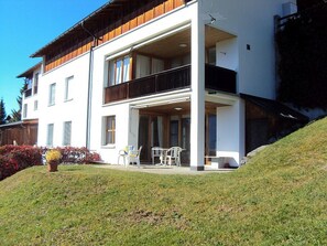 A two-story building with a balcony, outdoor seating, and a grassy slope. - Plattas, (Flims Fidaz), 1045 by Interhome (Flims)