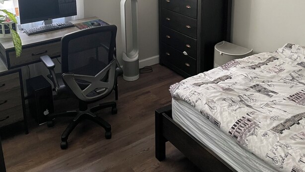 Un dormitorio con cama, escritorio con computadora, silla, cómoda y radiador.