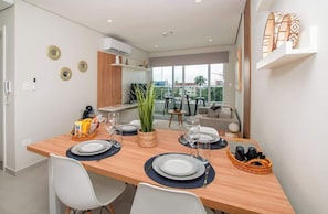 A modern dining area with a wooden table set for four, a plant, and a view of the city. - Corporate Stays First Living - 102 (Asunción)