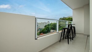Ein Balkon mit Glasgeländer, einem kleinen Tisch und vier schwarzen Stühlen.