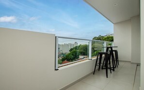 A balcony with a glass railing, a small table, and four black chairs. - Corporate Stays First Living - 102 (Asunción)