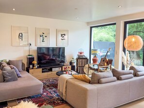 Ein modernes Wohnzimmer mit großem Flachbildfernseher, bequemen Sofas, einem Couchtisch und einem gemusterten Teppich.