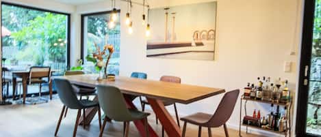 A modern dining area with a large wooden table, multiple chairs, and a hanging light fixture.