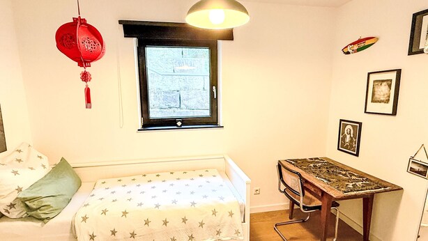 Ett sovrum med en säng, ett skrivbord, ett fönster och en hängande lampa.