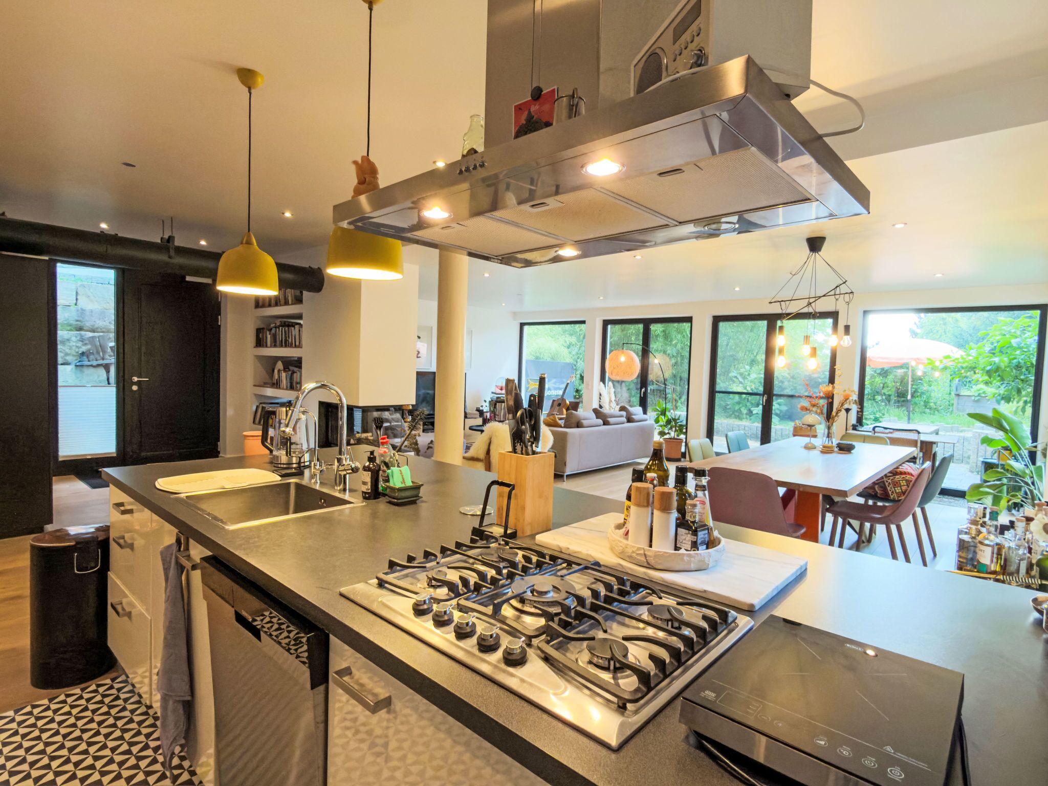 Une cuisine moderne dotée d’un îlot central, d’appareils électroménagers en acier inoxydable et de luminaires suspendus.