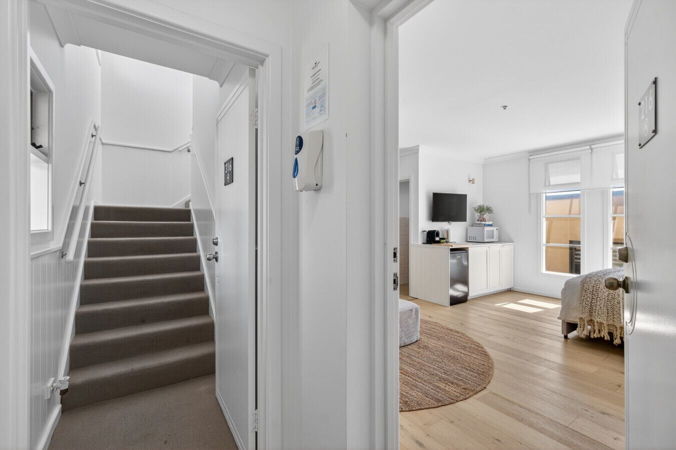 A modern interior with a staircase, a kitchen area, and a living space with a large window.