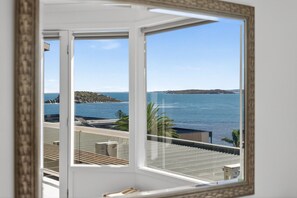 Ein Zimmer mit großem Fenster und Blick auf die Küste, einschließlich eines Gewässers und Land im Hintergrund.