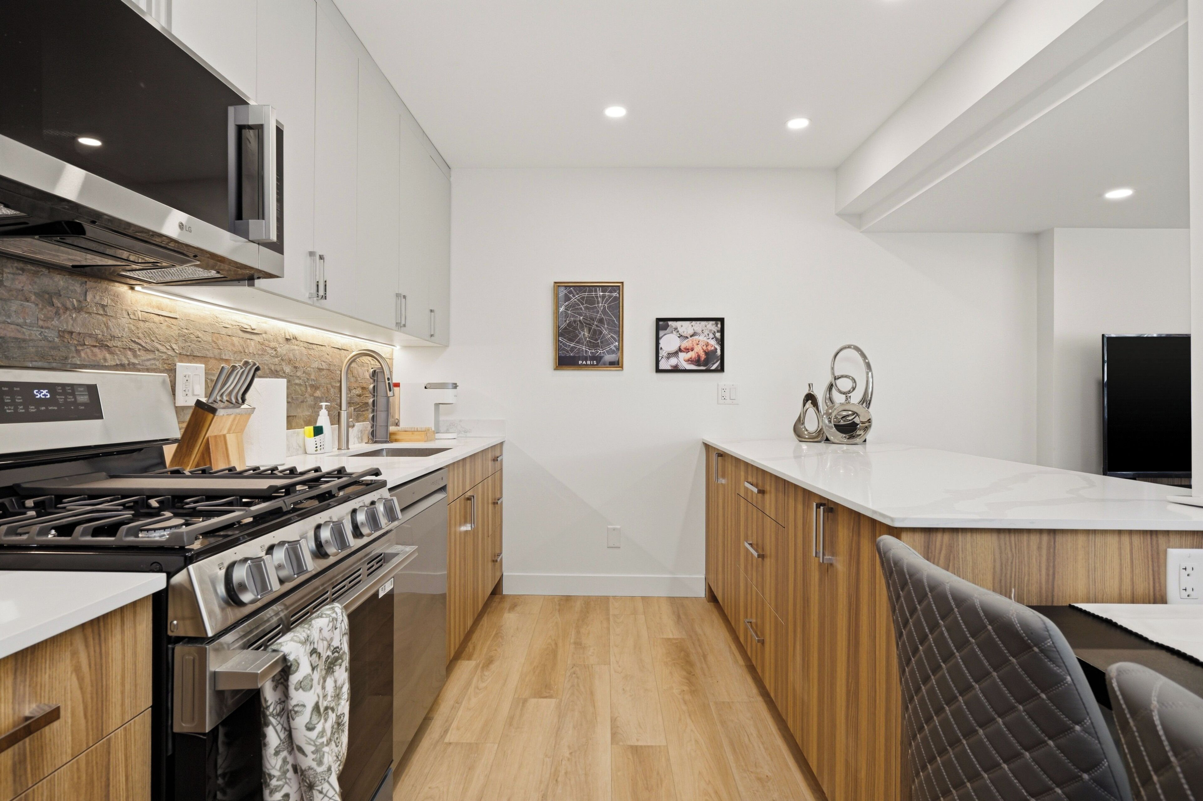 A modern kitchen with a gas stove, oven, and microwave. There are wooden cabinets and a white countertop.