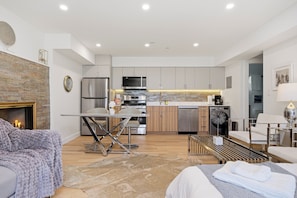 A modern kitchen with stainless steel appliances, a dining area with a glass table, and a cozy seating area with a fireplace. - Modern 3BR 2BA West Van near Dundarave Beach (West Vancouver)