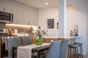 A modern kitchen with a dining area, featuring a green vase with flowers, a microwave, and a stove. - Modern 3BR 2BA West Van near Dundarave Beach (West Vancouver)