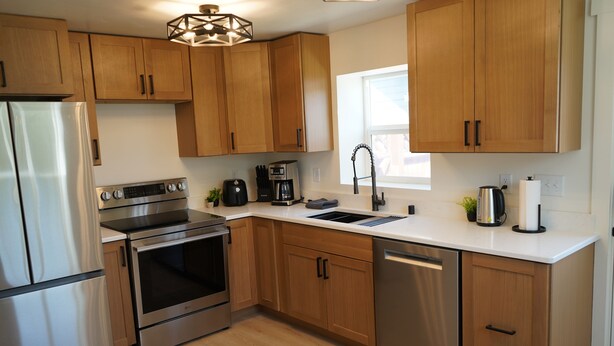 A modern kitchen with stainless steel appliances, wooden cabinets, and a white countertop.