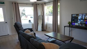 A living room with a sofa, a coffee table, a TV on a stand, and a view of the outside.