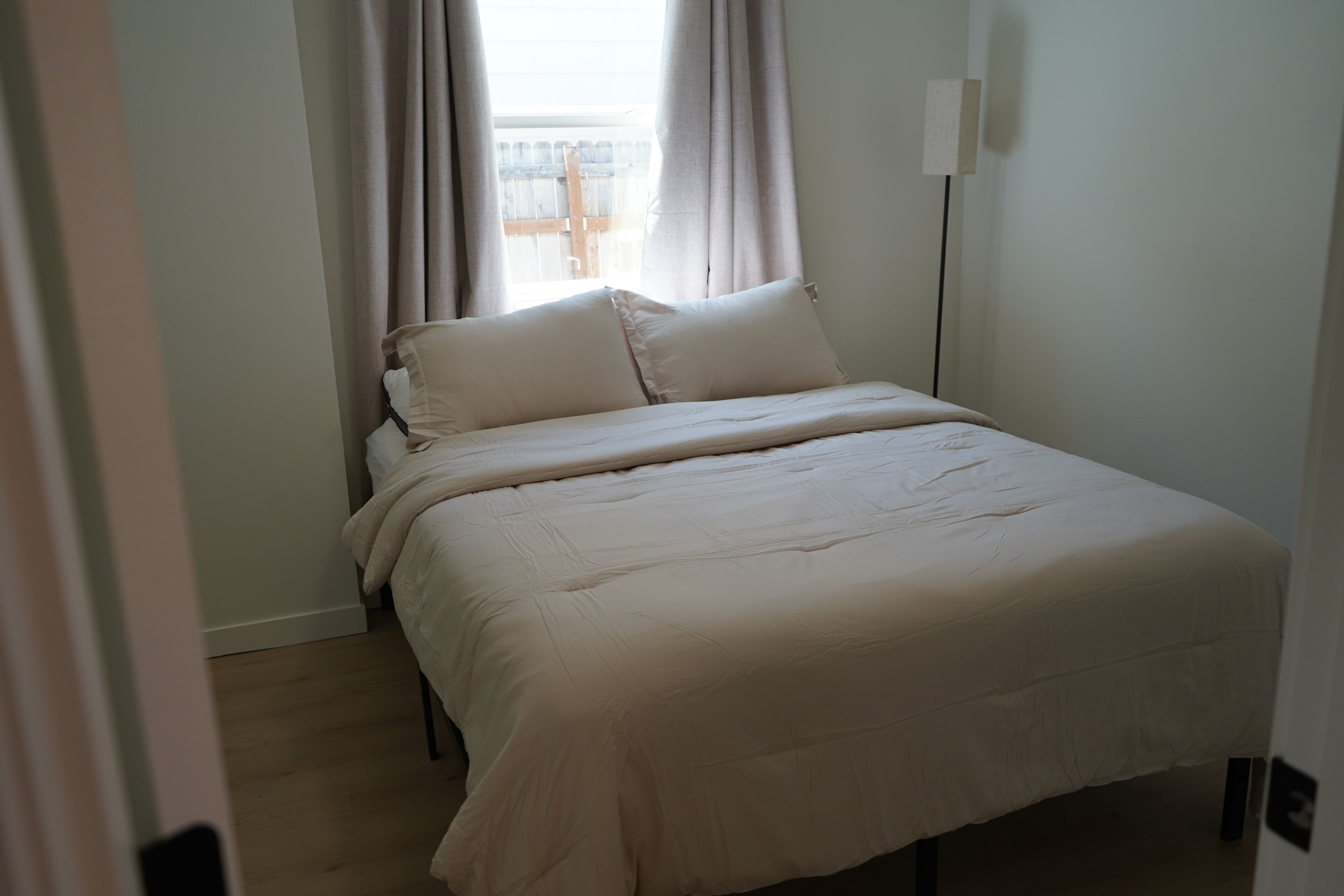 Un dormitorio con cama, cortinas y una lámpara de noche.