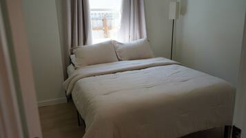 Un dormitorio con cama, cortinas y una lámpara de noche.