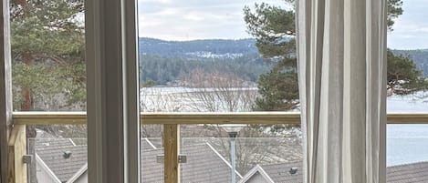 A view from a window with a metal railing, overlooking a snowy landscape with trees and houses.