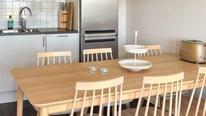 A modern kitchen with a wooden dining table, chairs, a stainless steel refrigerator, and a toaster.