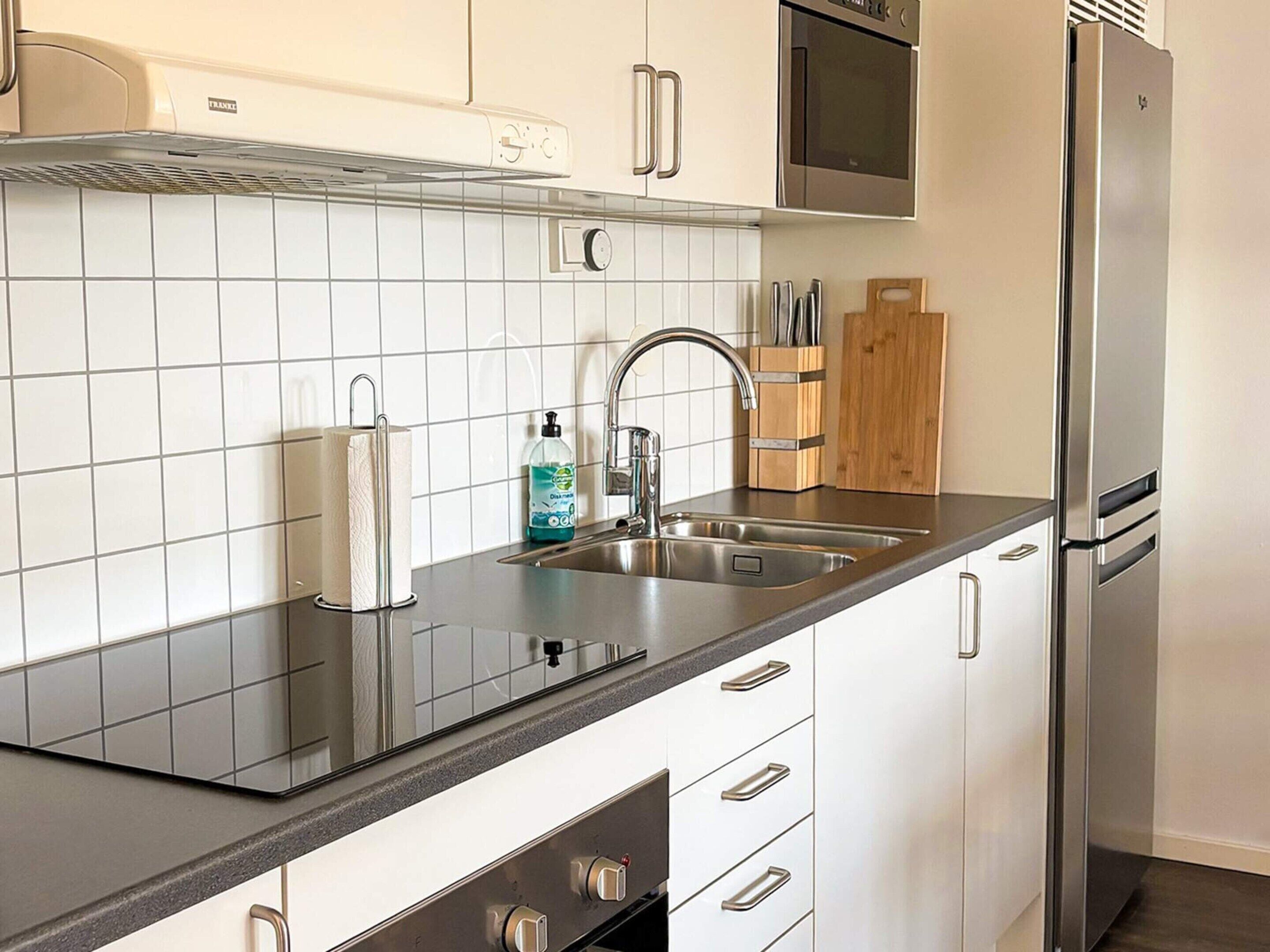 A modern kitchen with a stainless steel refrigerator, double sink, and white cabinetry.