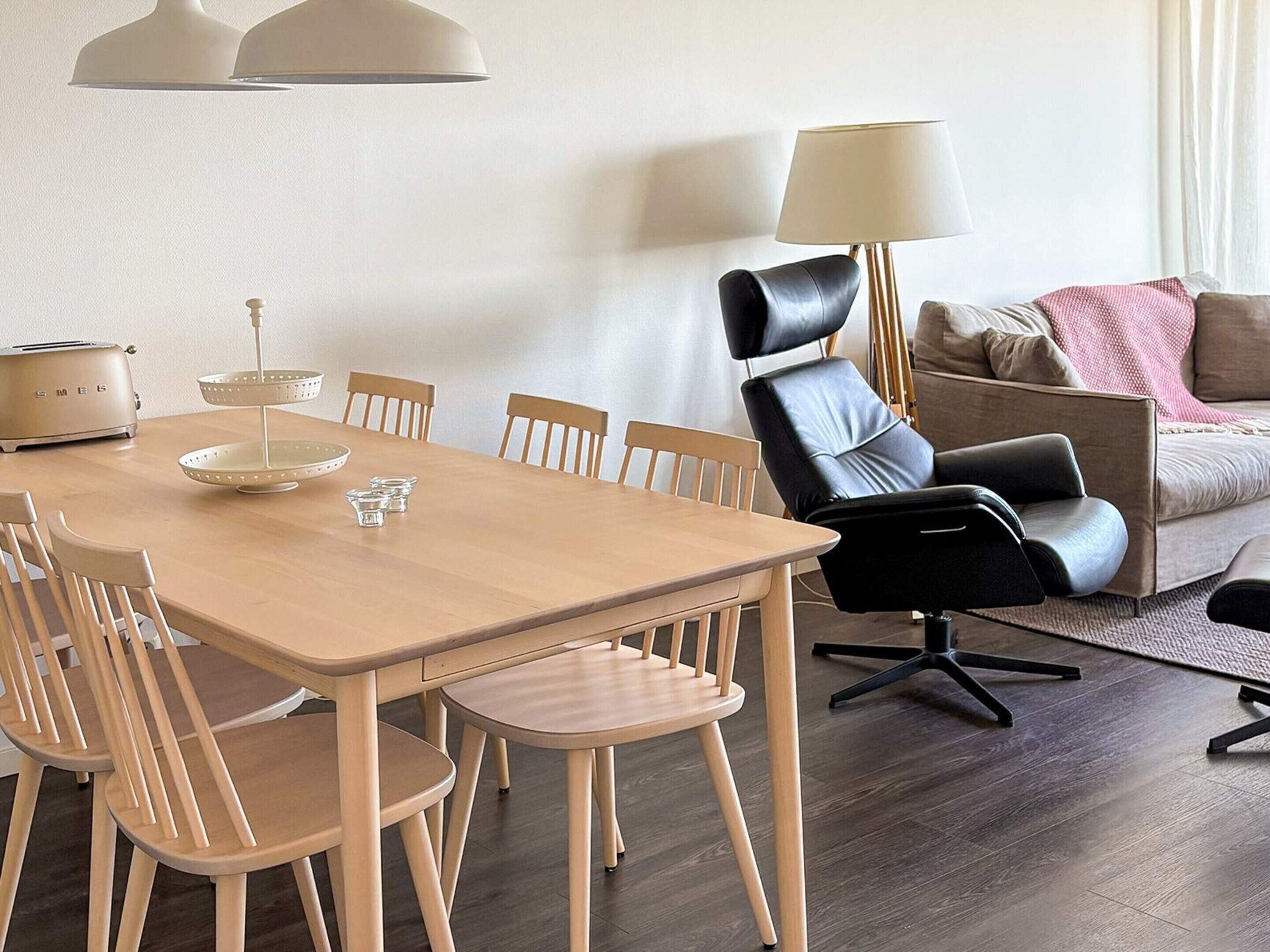 A modern living room with a dining area, featuring a wooden dining table, chairs, a sofa, and a floor lamp.