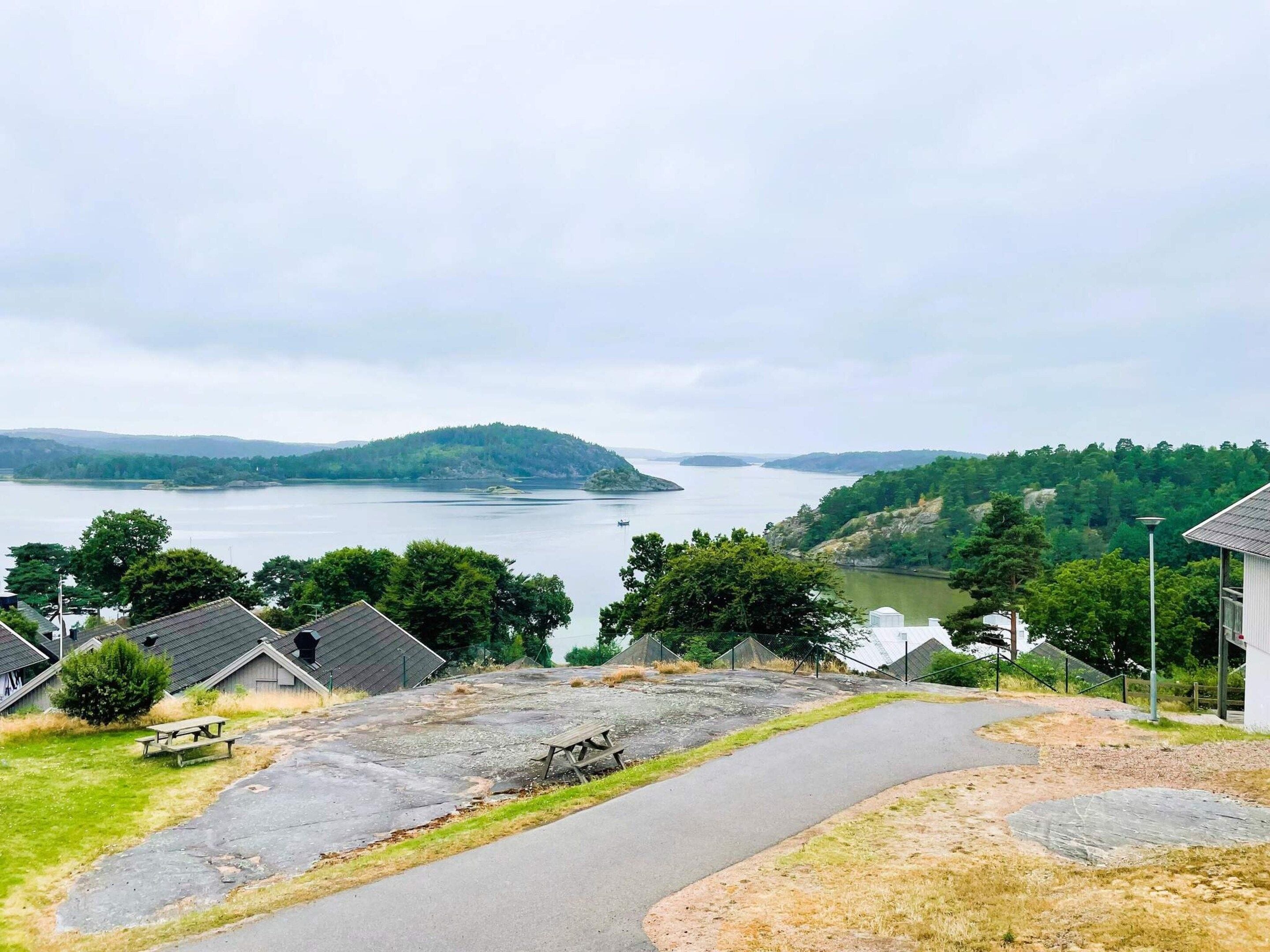 A lakeside property with a paved walkway, picnic tables, and a view of a lake and distant hills.