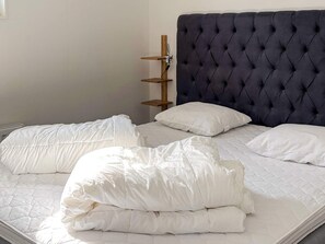 A bed with a tufted headboard, white bedding, and a wooden shelf unit beside it. - 5 Star Holiday Home in Uddevalla (Uddevalla)