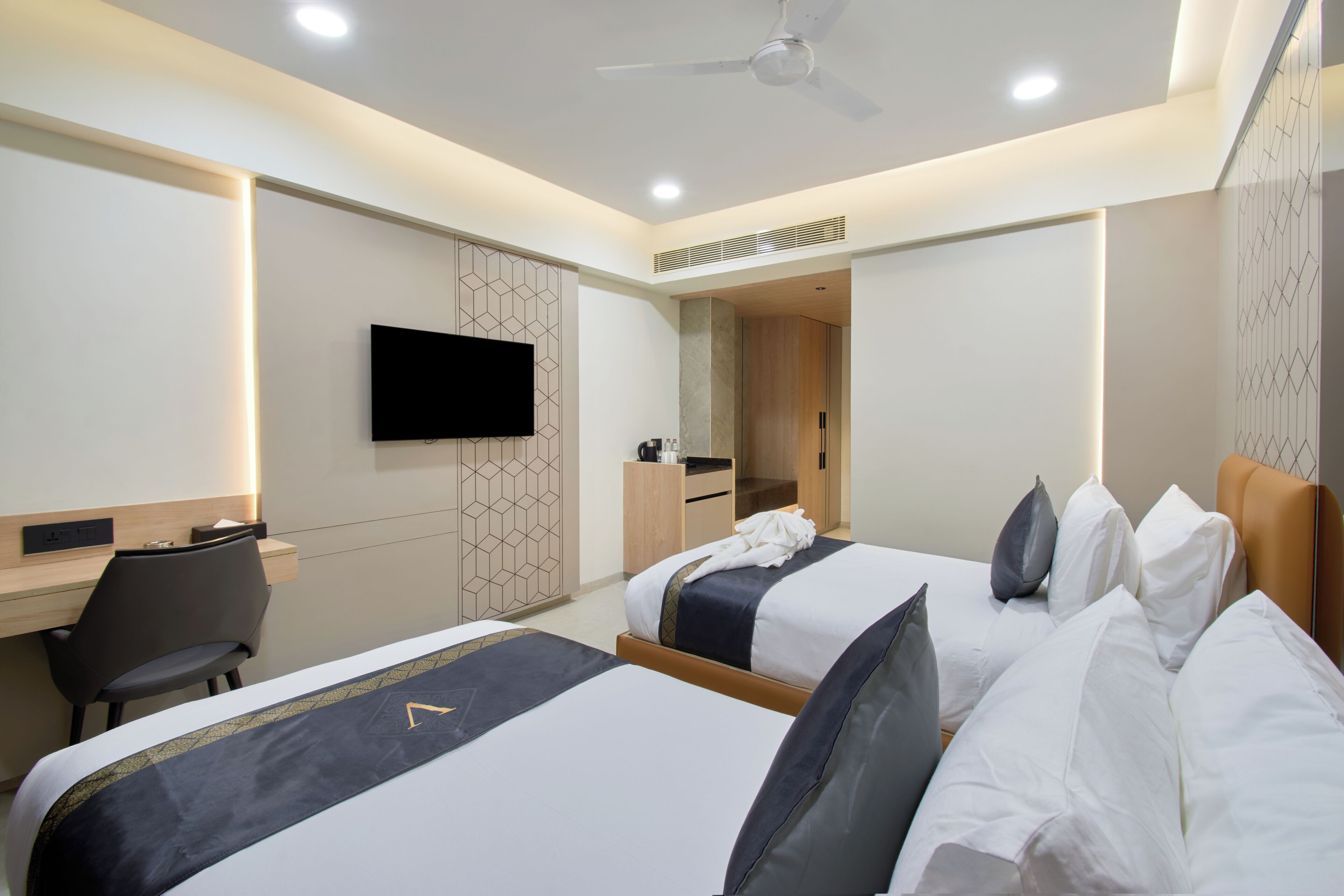 A hotel room with two beds, a desk, a television, and a ceiling fan.