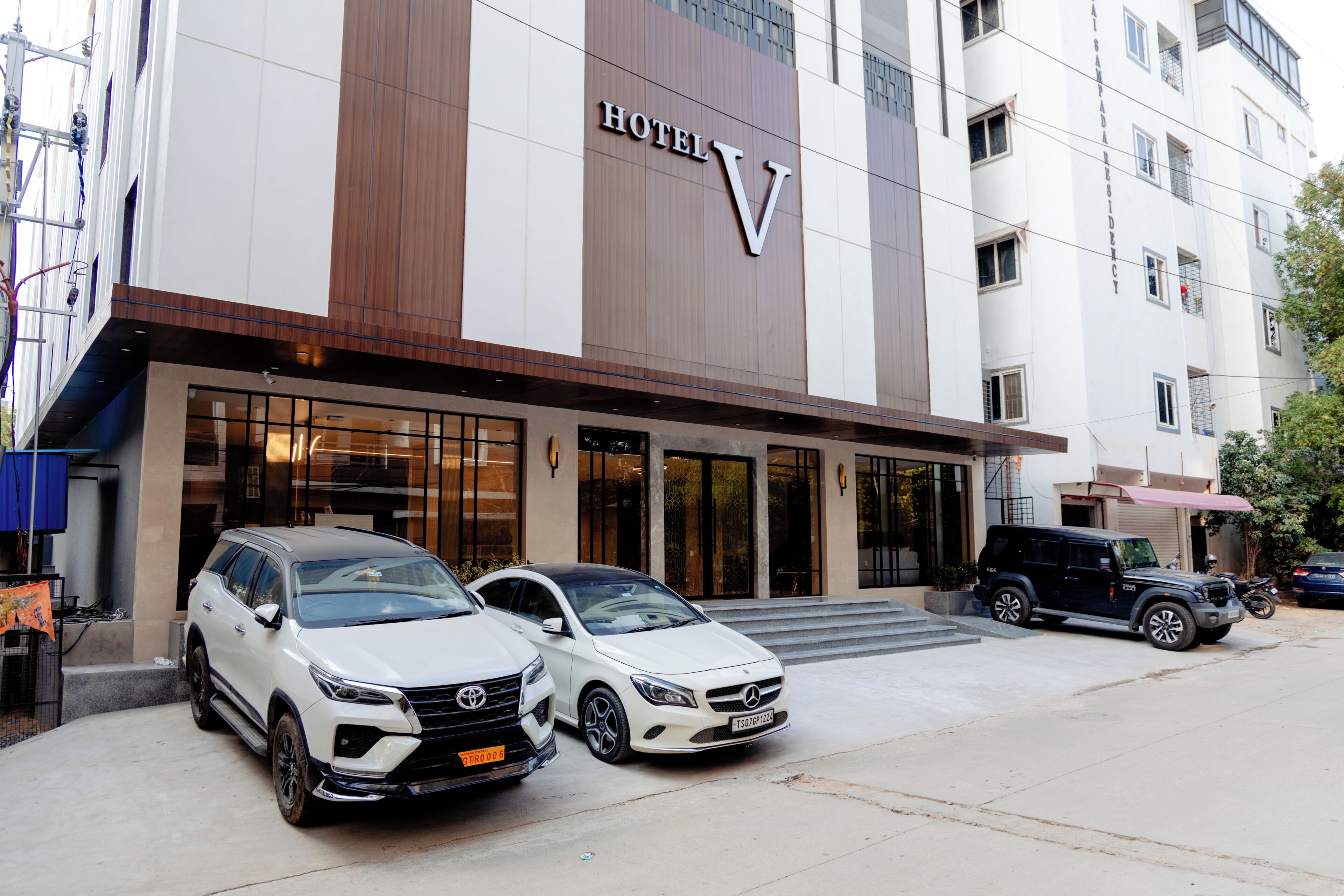 A hotel with a prominent 'V' sign, two parked SUVs, and a motorcycle.