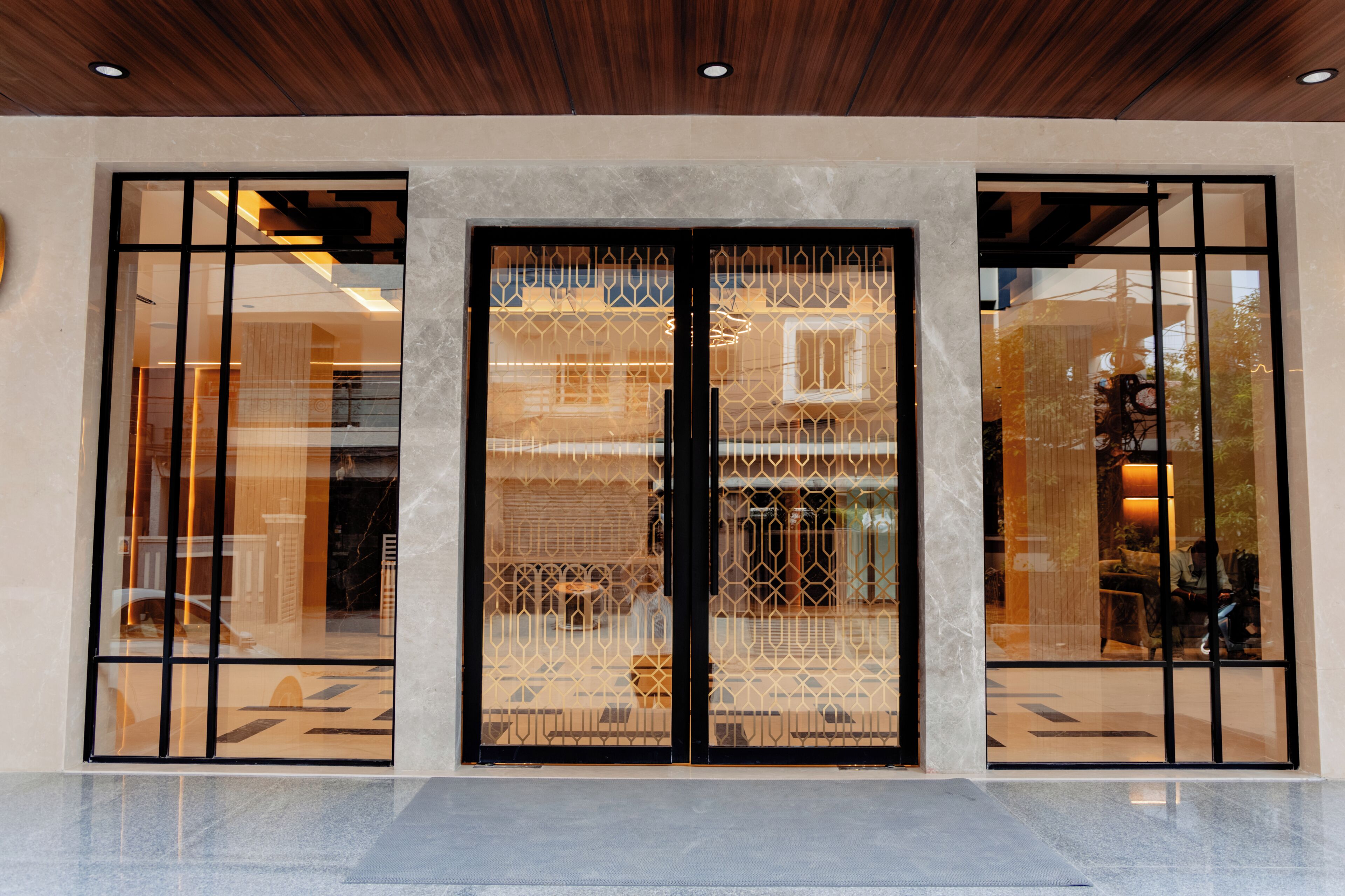A building entrance with a large glass door and windows, a wooden ceiling, and a tiled floor.
