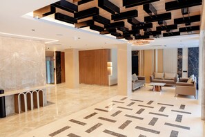 A modern lobby with a marble floor, a reception desk, a seating area with sofas, and a wooden accent wall. - ECKO Premier V Kondapur (Hyderabad)