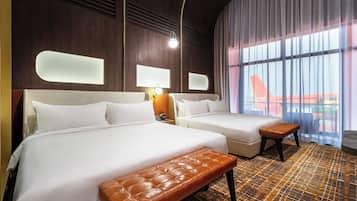 A hotel room with two beds, a bench, a nightstand, and a large window with a view.